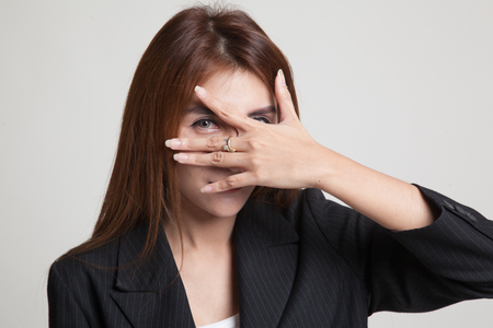 Beautiful young Asian woman peeking through fingers on gray backgroundの写真素材