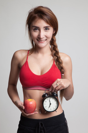 Beautiful Asian healthy girl with clock and apple on gray backgroundの写真素材
