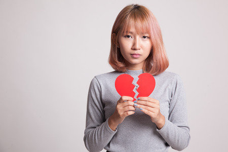 Beautiful young Asian woman with broken heart on gray backgroundの写真素材