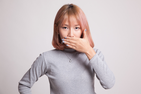 Young Asian woman close her mouth with hand on gray backgroundの写真素材