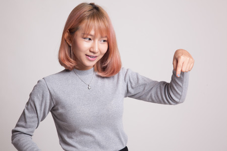 Beautiful young Asian woman point down to blank space on gray backgroundの写真素材