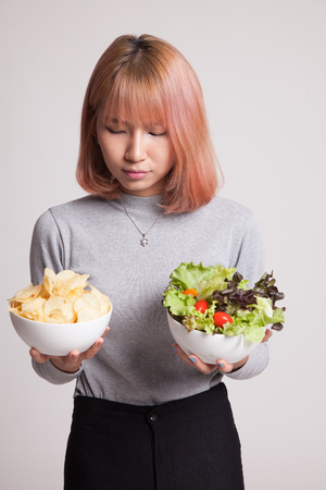 Young Asian woman with potato chips and salad on gray backgroundの写真素材