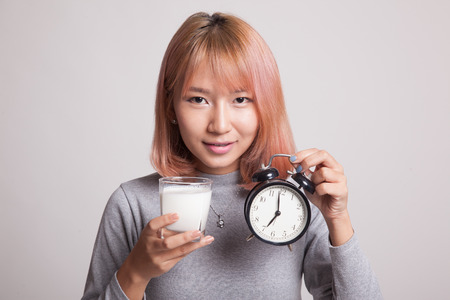 Healthy Asian woman drinking  glass of milk hold clock on gray backgroundの写真素材