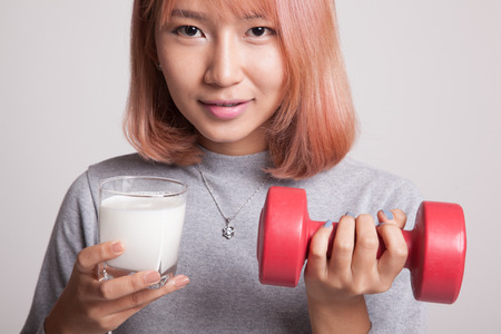 Healthy Asian woman drinking a glass of milk and dumbbell on gray backgroundの写真素材