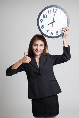Young Asian business woman thumbs up with a clock on gray backgroundの写真素材