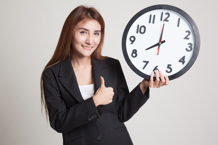 Young Asian woman thumbs up with a clock on gray backgroundの写真素材