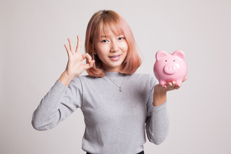 Asian woman show OK  with pig coin bank on gray backgroundの写真素材