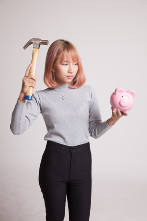 Asian woman with pig coin bank and hammer on gray backgroundの写真素材