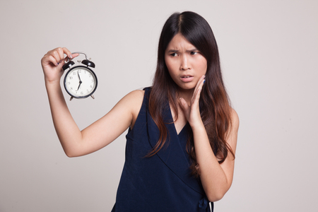 Young Asian woman is stressed with a clock on gray backgroundの写真素材