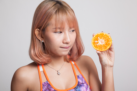 Beautiful Asian healthy girl with orange fruit licks her lips on gray backgroundの写真素材