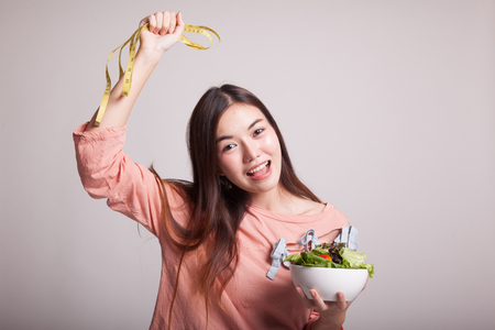 Healthy  Asian woman with measuring tape and salad on gray backgroundの写真素材