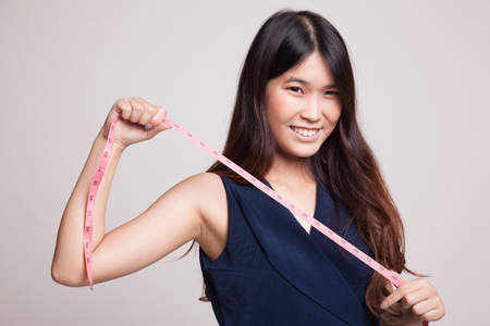 Young Asian woman with measuring tape on gray backgroundの写真素材