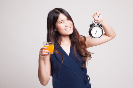 Asian woman with a clock drink orange juice on gray backgroundの写真素材