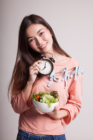 Young Asian woman with clock and salad on gray backgroundの写真素材
