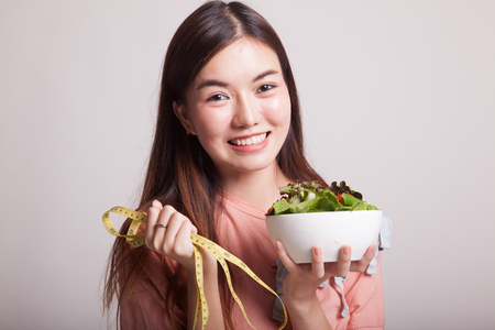 Healthy  Asian woman with measuring tape and salad on gray backgroundの写真素材