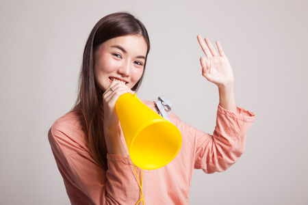 Beautiful young Asian woman show OK  announce with megaphone on gray backgroundの写真素材