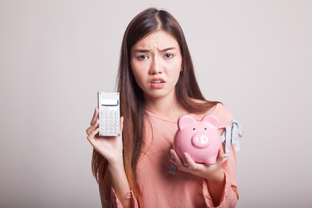 Unhappy Asian woman with calculator and piggy bank on gray backgroundの写真素材