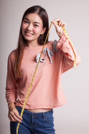 Young Asian woman with measuring tape on gray backgroundの写真素材
