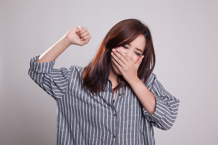 Sleepy young Asian woman yawn on gray backgroundの写真素材