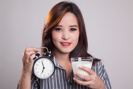 Healthy Asian woman drinking  glass of milk hold clock on gray backgroundの写真素材