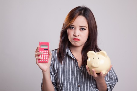 Unhappy Asian woman with calculator and piggy bank on gray backgroundの写真素材
