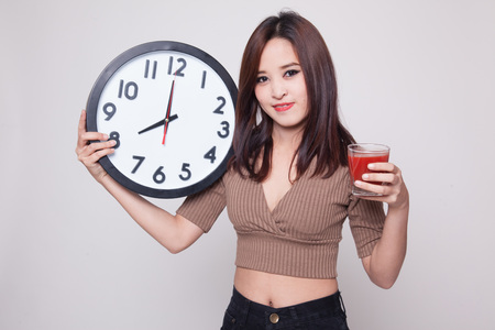 Young Asian woman with tomato juice and clock on gray backgroundの写真素材