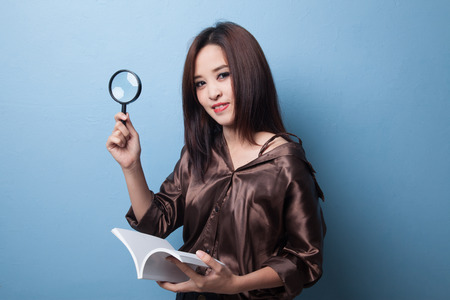 Asian woman with a book and magnifying glass on blueの写真素材