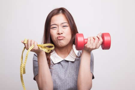 Exhausted  Asian woman with dumbbells and measuring tape on gray backgroundの写真素材