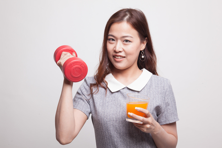 Young Asian woman with dumbbell drink orange juice on gray backgroundの写真素材