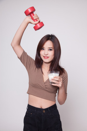 Healthy Asian woman drinking a glass of milk and dumbbell on gray backgroundの写真素材