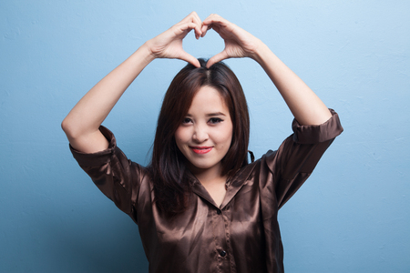 Young Asian woman gesturing heart hand sign on blue backgroundの写真素材