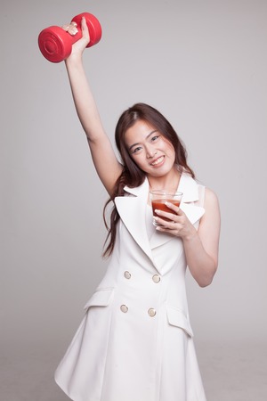 Young healthy Asian woman with dumbbell and  tomato juice on gray backgroundの写真素材