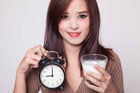 Healthy Asian woman drinking  glass of milk hold clock on gray backgroundの写真素材