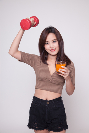 Young Asian woman with dumbbell drink orange juice on gray backgroundの写真素材