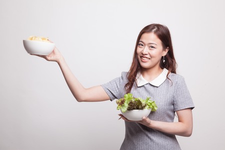 Young Asian woman with potato chips and salad on gray backgroundの写真素材