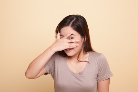 Beautiful young Asian woman peeking through fingers on beige backgroundの写真素材