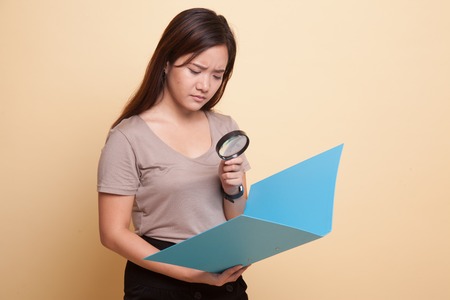 Young Asian woman with a magnifying glass check report on beige backgroundの写真素材
