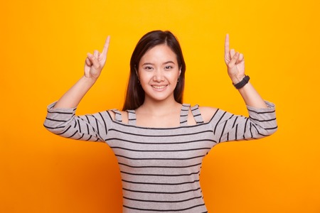 Young Asian woman point to blank space on yellow backgroundの写真素材