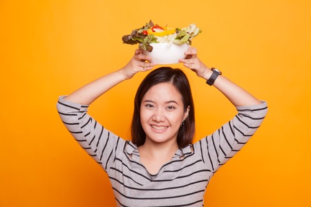 Healthy Asian woman with salad on yellow background