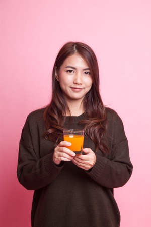 Young Asian woman drink orange juice on pink backgroundの写真素材