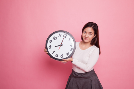Young Asian woman with a clock on pink backgroundの写真素材