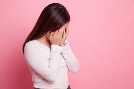 Sad young Asian  woman cry with palm to face on pink background