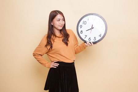 Young Asian woman with a clock on beige backgroundの写真素材