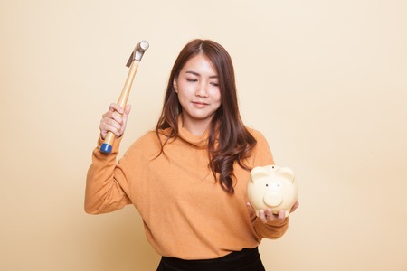 Asian woman with pig coin bank and hammer on beige backgroundの写真素材