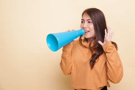 Beautiful young Asian woman announce with megaphone on beige backgroundの写真素材