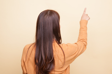 Back of Asian woman touching the screen with her finger on beige backgroundの写真素材