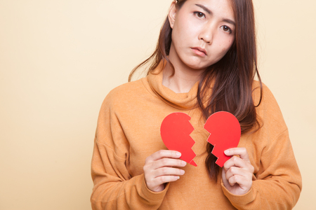 Beautiful young Asian woman with broken heart on beige backgroundの写真素材