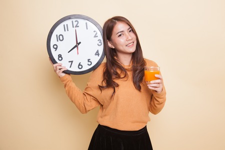 Asian woman with a clock drink orange juice on beige backgroundの写真素材