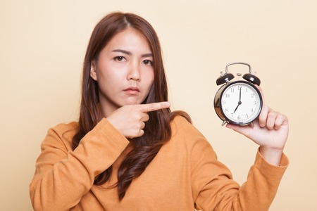 Angry young Asian woman point to a clock on beige backgroundの写真素材