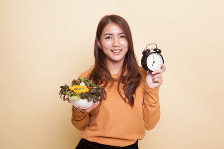 Young Asian woman with clock and salad on beige backgroundの写真素材